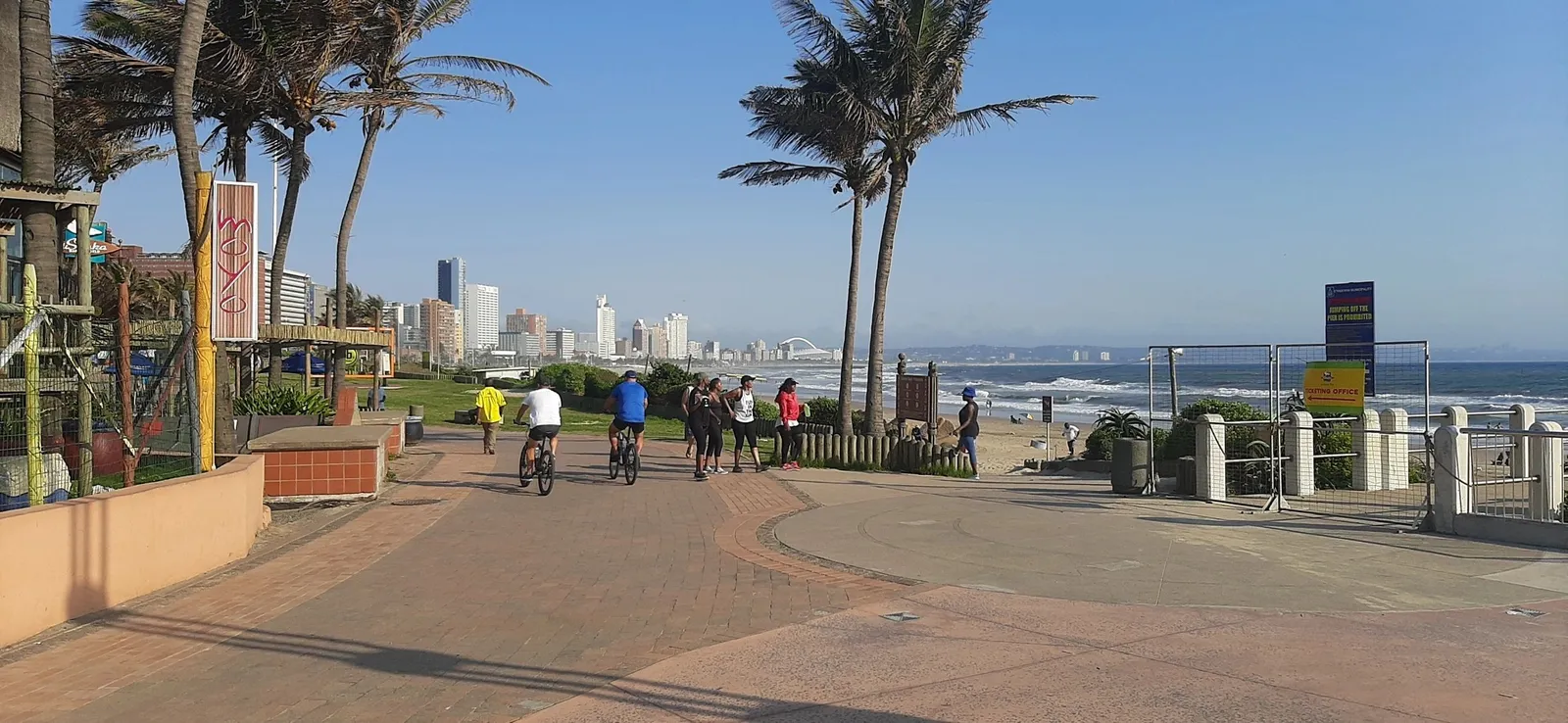 People biking and walking along a sunny beach promenade.